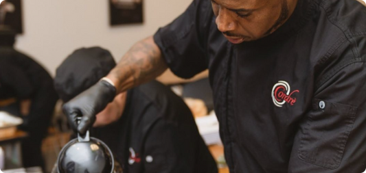 A chef is focused on crafting a black and white helmet, blending artistry with culinary expertise in an innovative dish.
